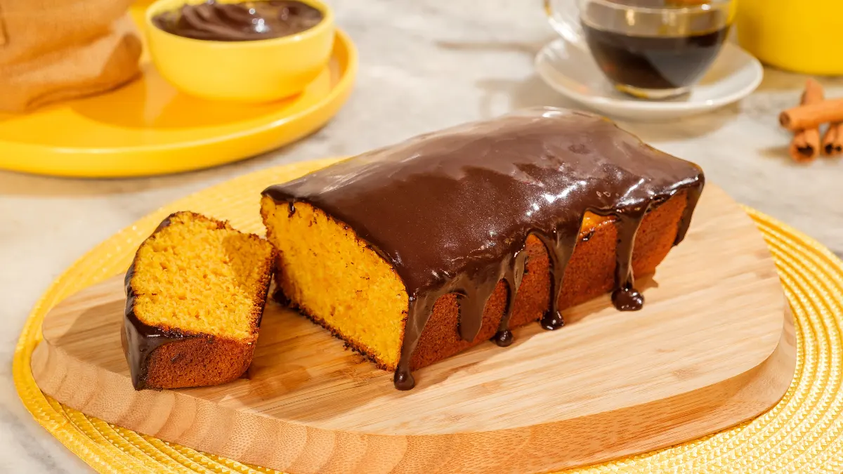 Fatia de bolo de cenoura fofinho servida em um prato com cobertura de chocolate crocante por cima.